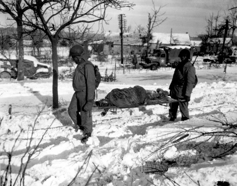 Body of American soldier is borne on stretcher from terrain in vicinity of Malmedy