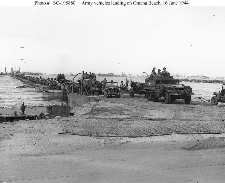 Army vehicles roll ashore on one of the floating causeways of the Mulberry artificial harbor